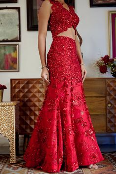 This structured red mermaid lehenga set personifies the emblem of romantic glamour. The set features intricate embroidery of cutdana work and dori with red sequins, beads, and floral applique work adorning both the skirt and blouse. Its focal point is the tassel detailing flowing at the bottom of the skirt with cute flower motifs made of sequins. • Sleeveless blouse with floral applique detailing highlighted with nalki crystals and beads.• Blouse contains a metal hook on the front side.• Heavily embroidered dupatta with botanical motifs detailing accentuated with sparkling sequins and crystals. • Lehenga skirt adorned with floral applique handwork detailing and drop-down tassels adorning the bottom of the skirt. • Lehenga contains a left zipper for support along with a metal hook.From Mole Glamorous Gown With Intricate Embroidery For Festive Occasions, Glamorous Gown With Saree Shape And Intricate Embroidery, Glamorous Gown With Intricate Embroidery In Saree Style, Fitted Evening Dress With Intricate Embroidery For Festive Occasions, Red Party Wear Lehenga With Intricate Embroidery, Glamorous Semi-stitched Floor-length Gown, Glamorous Embroidered Party Lehenga, Floor-length Floral Embroidered Party Choli, Party Floral Embroidered Floor-length Choli