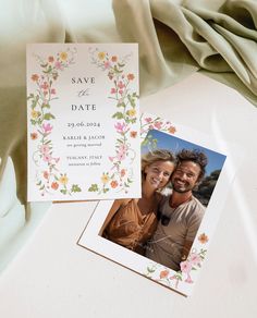 two wedding cards on top of a white tablecloth with flowers and leaves around them