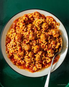 a white bowl filled with pasta and meatballs on top of a green tablecloth