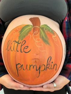 a pregnant woman holding a pumpkin with the words little pumpkin painted on it's belly