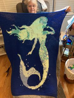 a woman holding up a crocheted blanket with a sea horse on the front