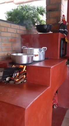 an outdoor kitchen with pots and pans cooking on the stove top, next to a brick wall