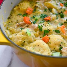 a pot filled with chicken and dumplings on top of a yellow table cloth next to a red napkin