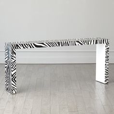 a zebra print bench sitting on top of a hard wood floor next to a white wall