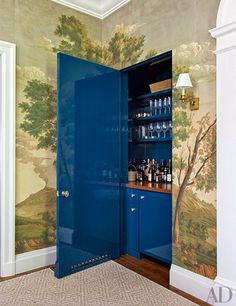 a blue cabinet with wine glasses on it in a room that is decorated with wallpaper