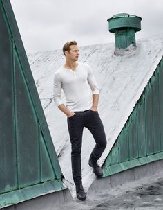 a man standing on top of a snow covered slope wearing a white shirt and black pants