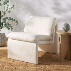 a white chair sitting on top of a rug next to a table and potted plant