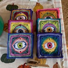 four square crocheted coasters sitting on top of a white tablecloth with colorful designs