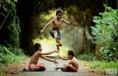 three boys playing on the side of a road with trees and bushes in the background