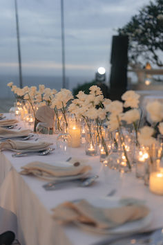 the table is set with candles and white flowers in glass vases on each side