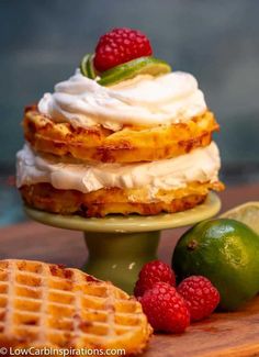 a stack of waffles topped with whipped cream and raspberries next to lime wedges