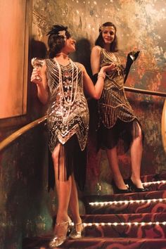 two women dressed in flappers and gats standing on stairs