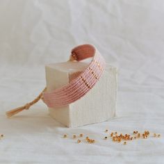 a white box with pink ribbon and gold beads on it next to some seed grains