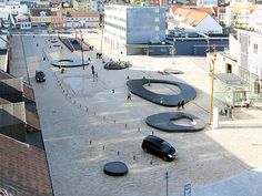 an aerial view of a city with cars parked on the ground and people walking around