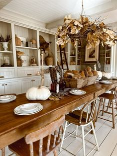 a wooden table topped with lots of white plates and bowls under a chandelier