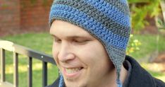 a man wearing a blue and gray knitted beanie smiles at the camera with his eyes closed