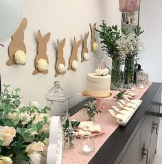 a table topped with cakes and flowers next to bunnies hanging from the wall behind them