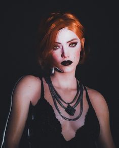 a woman with red hair and black makeup is posing for a photo in the dark