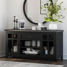 a black buffet table with plates and cups on it in front of a round mirror