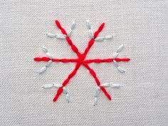 a red and white snowflake made out of yarn sitting on top of a piece of cloth