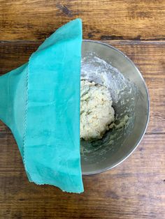 a metal bowl filled with dough on top of a wooden table next to a blue napkin