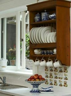 a wooden cabinet filled with plates and cups on top of a counter next to a sink