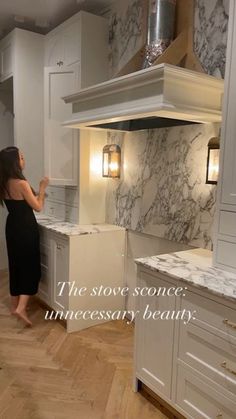 a woman in a black dress standing next to a white kitchen with marble counter tops