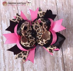 a leopard print hair bow with black and pink ribbon on top of a wooden surface