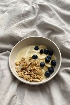 a bowl filled with cereal and blueberries on top of a white sheet covered bed