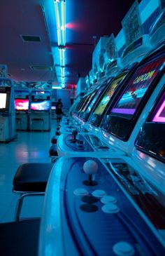 a row of video game machines in a room with blue lights and white tile flooring