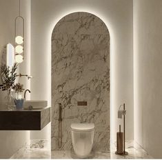 a white toilet sitting next to a sink in a room with marble walls and floor