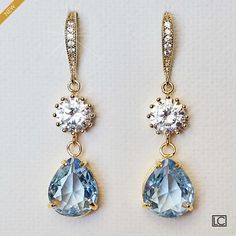 two pairs of earrings with blue and white stones hanging from gold hooks on a white surface