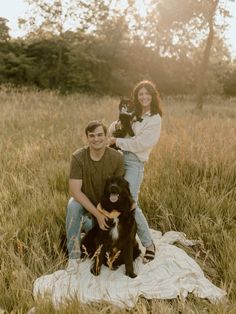 a man and woman are sitting on a blanket with their two dogs in the grass