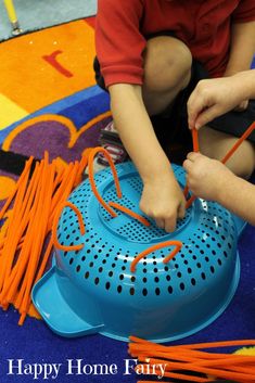 a young boy is playing with some orange string on a blue plastic object in the floor