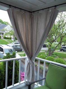 a balcony with green chairs and curtains on the windowsill, looking out onto a parking lot