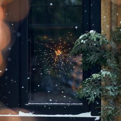 a firework is seen through the window of a house in winter time with snow on the ground