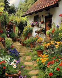 a garden filled with lots of flowers next to a white building on a dirt road