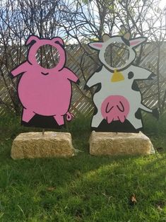 two wooden cut outs with pig and cow designs on them sitting in the grass next to a fence