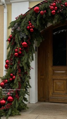 a christmas garland with red ornaments and greenery on the outside of a door way