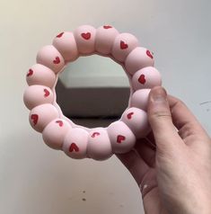 a hand holding a pink bracelet with hearts on it and a mirror in the background