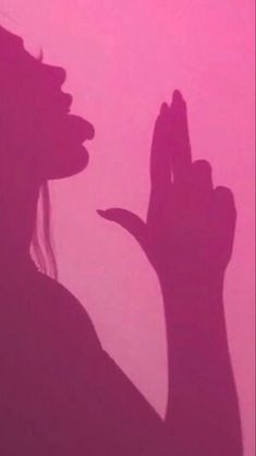 the silhouette of a woman holding her hand up in front of a pink sky background