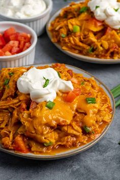 two plates filled with shredded chicken and topped with sour cream, tomatoes and green onions