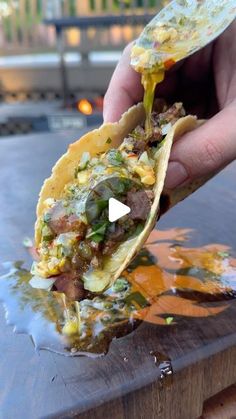 a person is holding up a taco with meat and vegetables in it on a wooden table