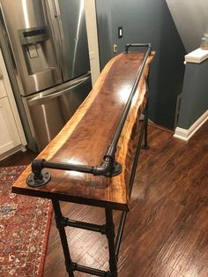 a wooden table sitting on top of a hard wood floor next to a metal refrigerator