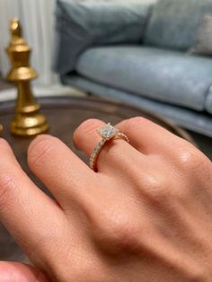 a person's hand with a diamond ring on their finger, in front of a couch