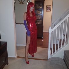 a woman in a red dress and blue gloves standing next to a stair case with a handbag on it