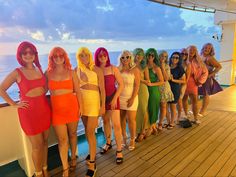 a group of women standing next to each other on top of a wooden deck near the ocean