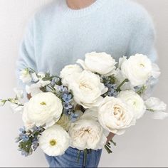 a woman holding a bouquet of white flowers in her hands and wearing a blue sweater