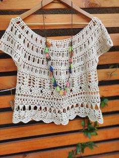 a white crocheted top hanging on a wooden hanger with beads attached to it