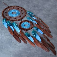 a blue and brown dream catcher with feathers on the floor next to another piece of wood